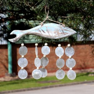 Bluewashed fish driftwood windchime with natural capiz shells hanging in a bright garden setting. A soft coastal touch for relaxed living spaces.