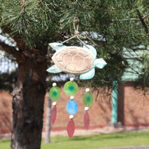 Handcrafted aqua turtle driftwood windchime with capiz shell drops hanging in a garden setting. Soft coastal windchime design bringing relaxed summer ambience.