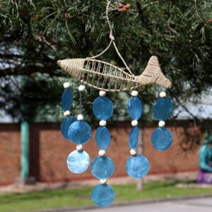 Handmade driftwood fish wind chime with natural capiz shell hanging in a bright garden setting. A gentle coastal accent for relaxed Irish living.