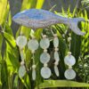 Bluewashed fish driftwood windchime with natural capiz shells hanging in a bright garden setting. A soft coastal touch for relaxed living spaces.