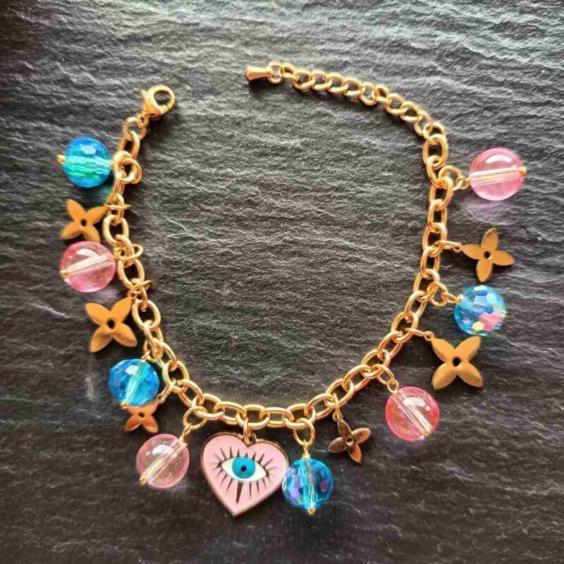 A playful and stylish bracelet featuring pink and blue glass beads, stainless steel over gold floral charms, and a heart evil eye centre piece for protection and good vibes. Handmade In Ireland with tracked An Post delivery.